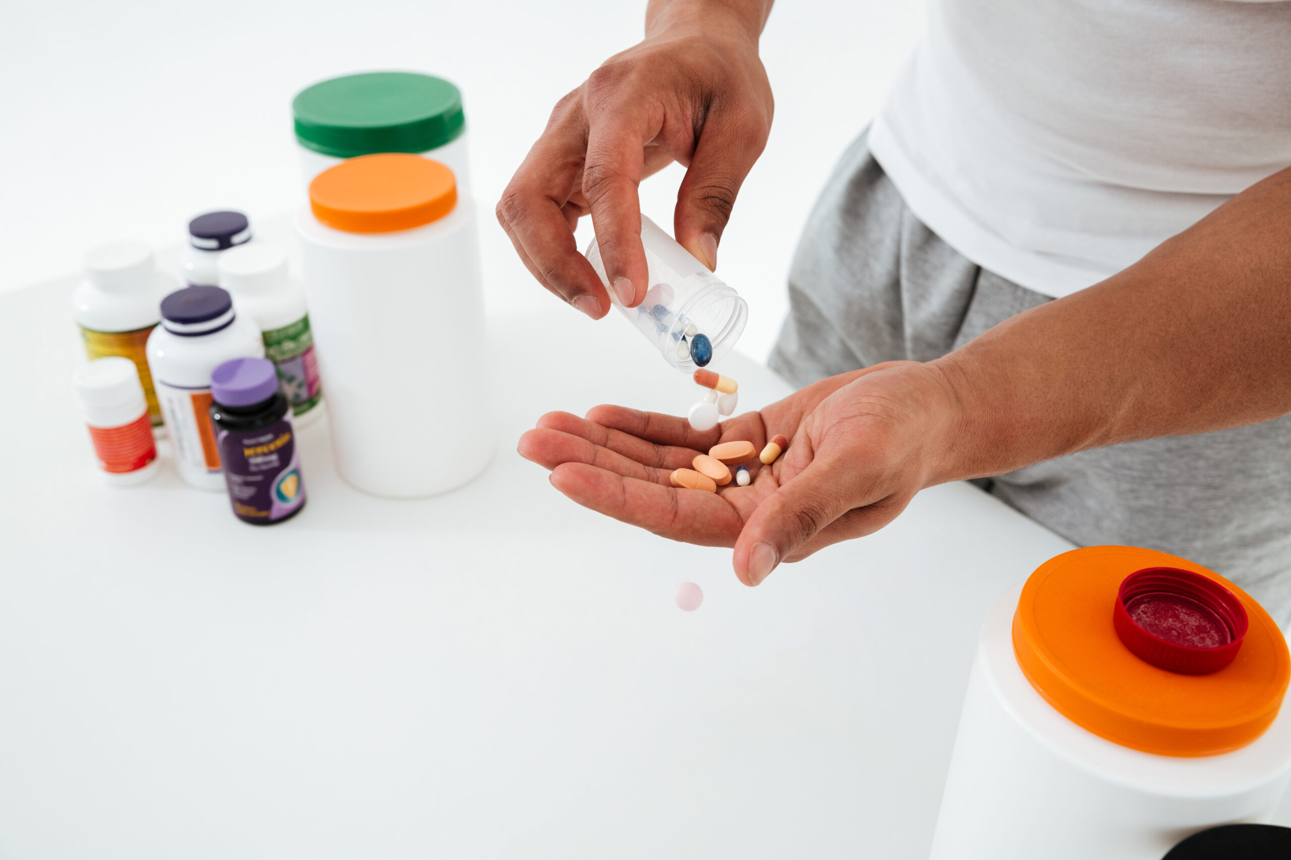 Cropped image of young sportsman standing over white background holding vitamins and sport pills.